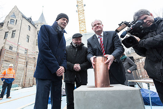 Oberbürgermeister Dr. Bernd Wiegand (li.), Rektor Prof. Axel Müller-Schöll (Mi.) und Staatssekretär Jörg Felgner (r.) versenken in dem Grundstein eine Zeitkapsel, gefüllt unter anderem mit einer Urkunde, einer aktuellen Tageszeitung und dem Katalog 